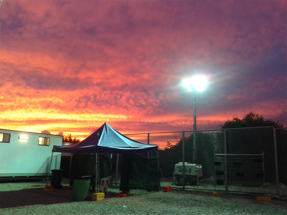 3 May 2015 at the single female's area in Nauru Regional Processing Centre 3: A beautiful late evening sky with security fence, lighting and tent in the foreground. (photograph by Elahe Zivardar, reproduced with permission)