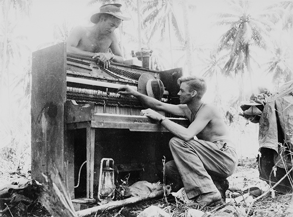 Australian solider trying to fix piano in jungle (photo courtesy of Australian War Memorial)